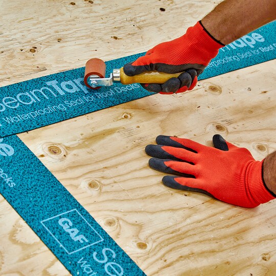 Roofer using roller to install GAF Roof Deck Seam Tape