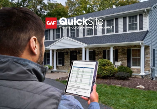 Contractor holding tablet in front of home open to QuickSite property data reports from GAF