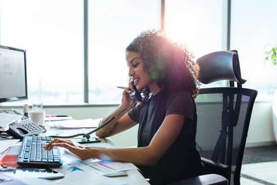 Women on phone at desk typing on a computer keyboard