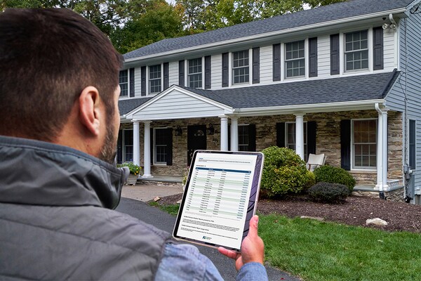 Contractor holding tablet in front of home open to QuickSite property data reports from GAF